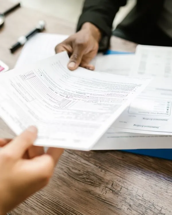 Dos personas intercambiando formularios sobre una mesa